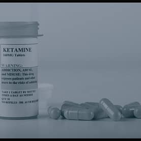 Ketamine prescription bottle with capsules on table beside it