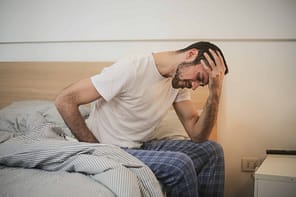 Tramadol Withdrawal as man sits on side of bed with head in hand looking to be sick.