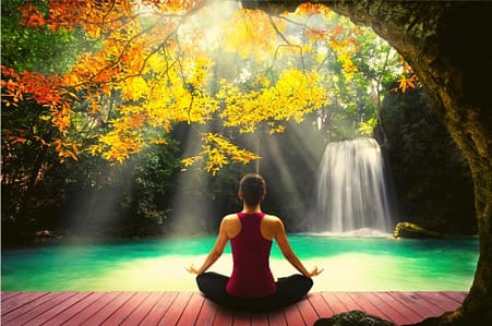 Image of beautiful waterfall with woman in front in meditative form to release anxiety.